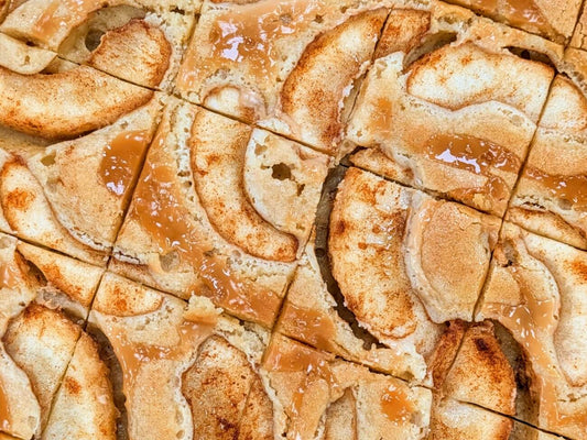 Overhead view of Buckabee Brownies Caramel Apple Blondie slab cut into squares, topped with caramel-glazed apple slices and cinnamon