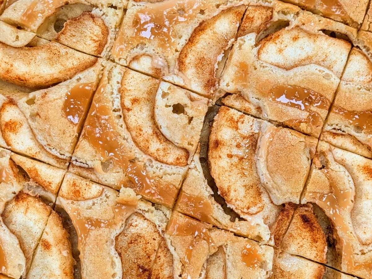 Overhead view of Buckabee Brownies Caramel Apple Blondie slab cut into squares, topped with caramel-glazed apple slices and cinnamon