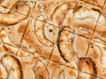 Overhead view of Buckabee Brownies Caramel Apple Blondie slab cut into squares, topped with caramel-glazed apple slices and cinnamon