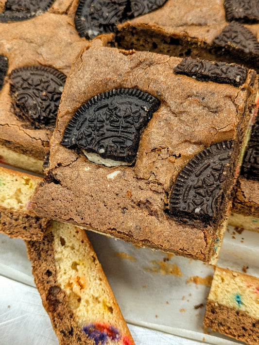 Close-up of sliced Cookies, Cream & Confetti Brookie showing dense Oreo-studded brownie top and colorful confetti blondie bottom layer