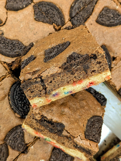 Spatula lifting a Cookies, Cream & Confetti Brookie square showing the layered Oreo brownie top and confetti blondie bottom surrounded by Oreo cookies