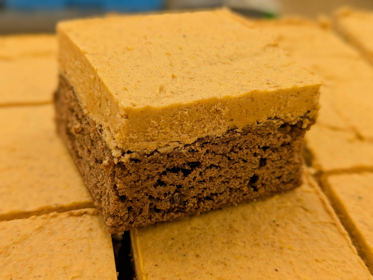 A fudgy chocolate brownie with pumpkin spice cream on top of other cut pumpkin brownies.