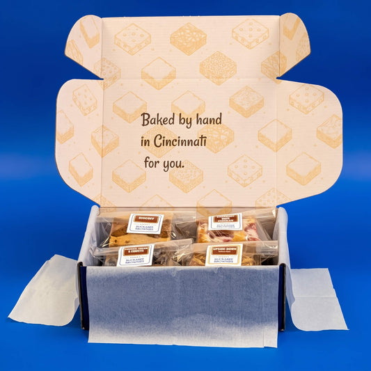 Open Buckabee Brownies box filled with individually wrapped treats, with “Baked by hand in Cincinnati for you” inside the lid.