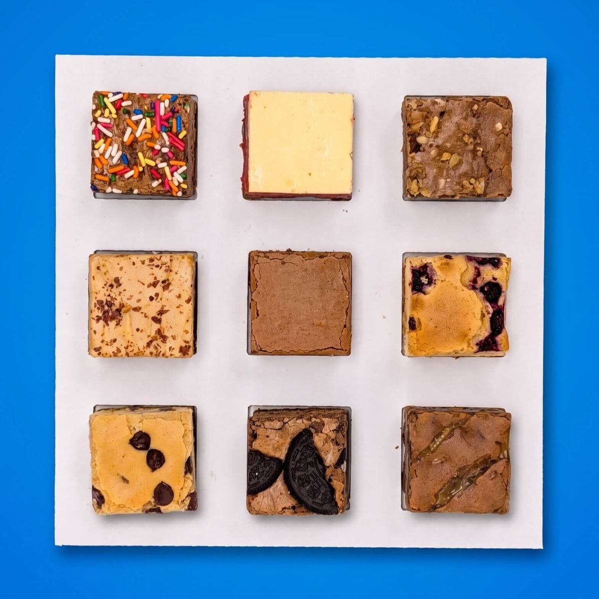 The Buckabee Experience Brownie Box - Nine square brownies arranged in a 3x3 grid The brownies include various flavors and toppings, such as chocolate chip, oreo cookie, walnut and sprinkles.