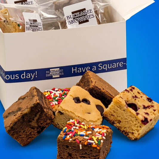 An open white gift box of Buckrabee Brownies' The Buckabee Experience Shipped Box with several brownie squares arranged in front on a bright blue background.